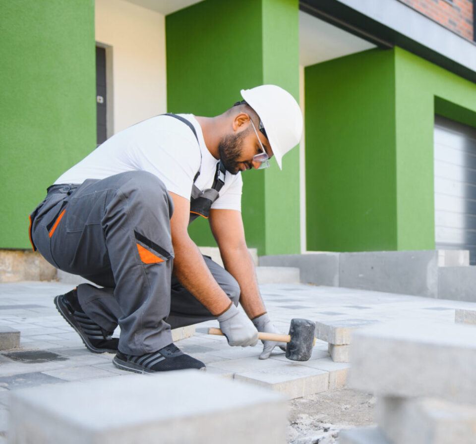 Indian Worker skillfully laying paving stones using a hammer and wearing gloves, showcasing precision.